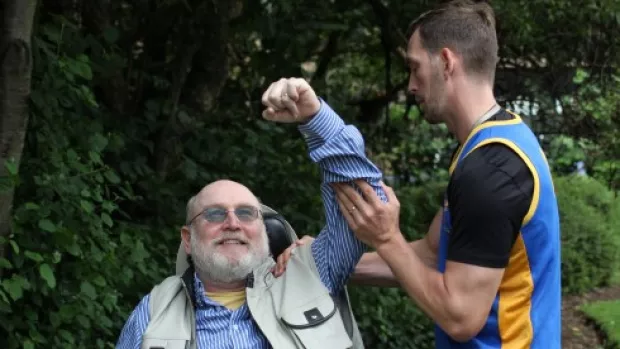 Picture shows a personal trainer helping a man with MS to stretch