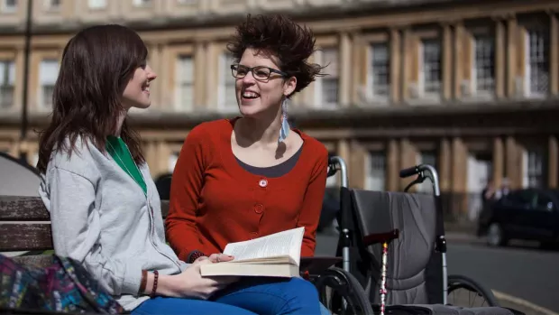 Photo: Young couple on bench reading and smiling with wheelchair