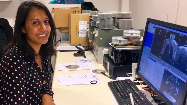 Anisha sits smiling at her desk, images of body scans on screen