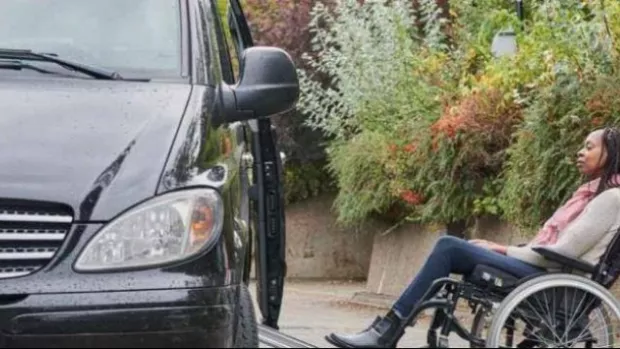 Woman using wheelchair is pushed up a ramp into a car