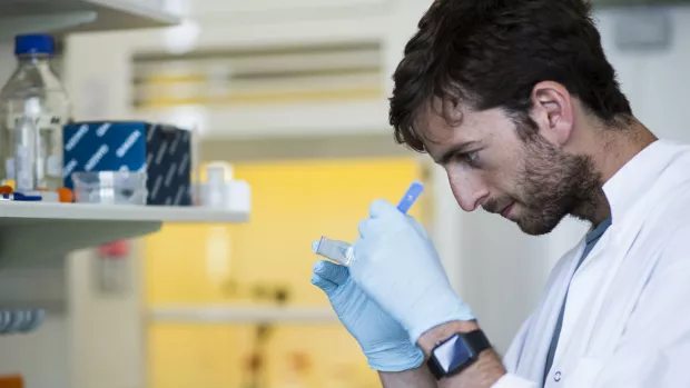 A young male scientist wearing a white lab coat and gloves works intently in a research lab.