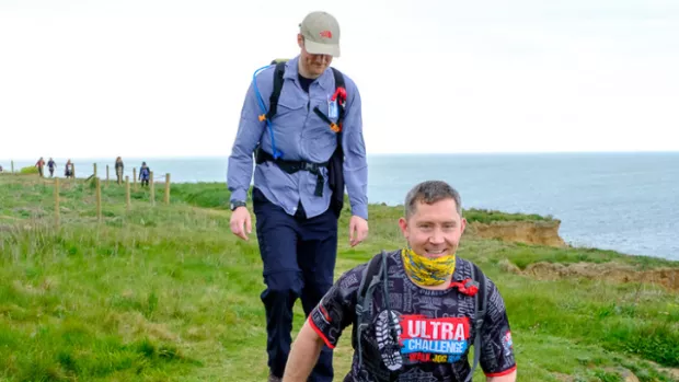 People wearing backpacks walking along a cliff pathway overlooking the sea