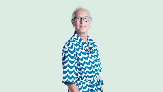 Jacquline with white hair and glasses stands in a blue and white print dress