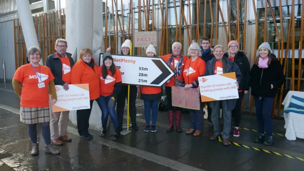 A group of MS Society campaigners stand outside the Scottish Parliment holding signs protesting against the Personal Independence Payment 20 metre rule