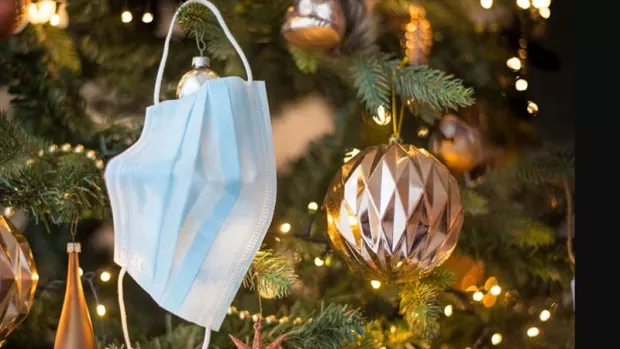 Close up of a surgical mask hanging with gold baubles on a real Christmas tree