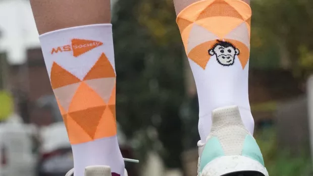 Crop of someone's ankles wearing socks with orange triangles. The left has an MS Society logo and the right has a monkey face.
