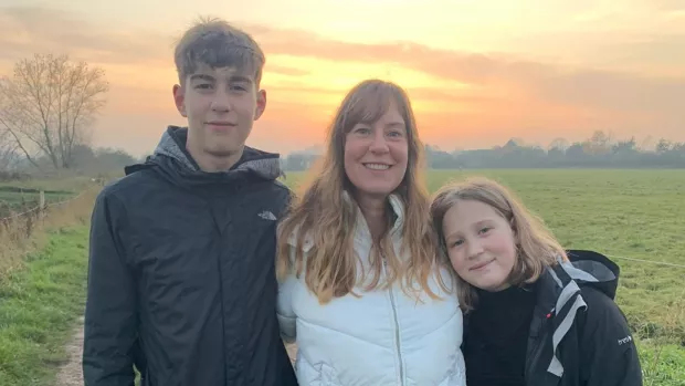 Emma stands with her son and daughter in a park, the sun setting behid them.