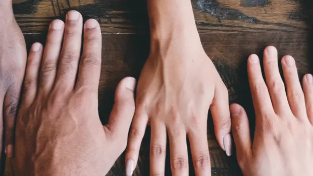 5 hands palms down on a wooden surface seen from above