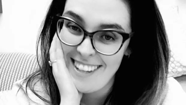 Black and white headshot of Laura smiling. She has long hair and glasses.