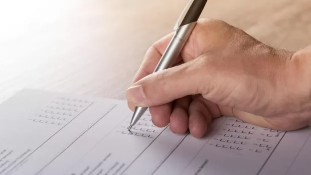 Image shows a hand holding a pen filling out a survey