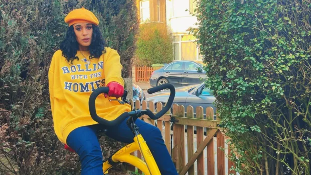 Roxanne sits on a bike. She's wearing a yellow beret and yellow sweatshirt. 