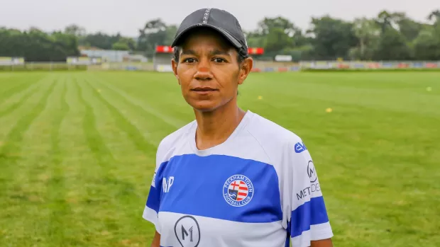 Mary stands on a football pitch wearing a football shirt and baseball cap.