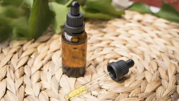 A brown glass bottle and a pipette filled with oil are on a grass mat