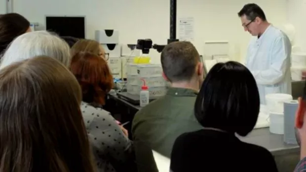 An audience watches a scientist wearing a white coat in the lab