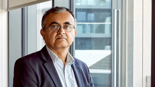 A man in a dark blue suit and glasses is next to a window