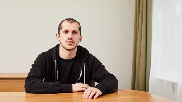 A man  sat at a desk in front of a white wall. 