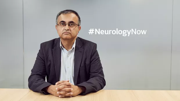 Waqar in suit sitting looking serious at a desk. Image includes Neurology Now hashtag