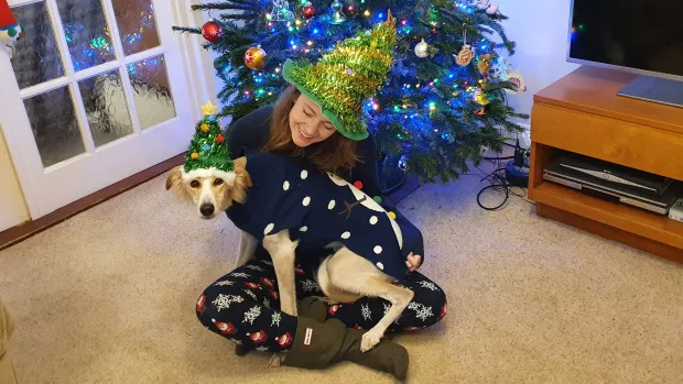 Photo of Catherine sitting on the floor with her dog in Christmas clothing