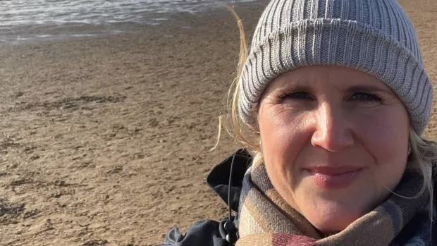 Head and shoulders image of Beccy on a beach wearing a woolly hat