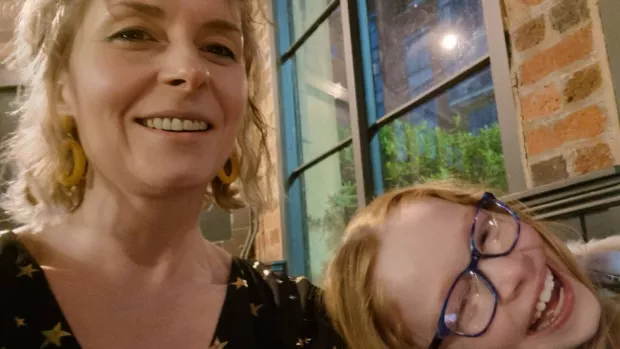 Beck smiles to camera, her daughter rests her head on her shoulder and is also smiling.