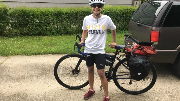 A photo shows Gina dressed in her cycling gear, leaning against her black bike outside