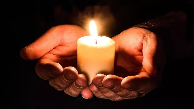 Hands cupping a lit candle 