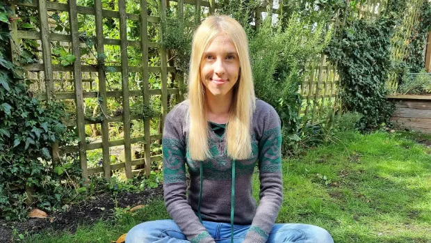 Heather sits cross legged in a garden