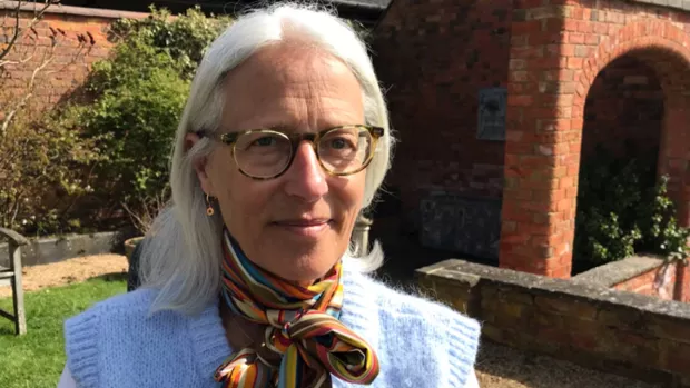 Jacqueline head shot with garden behind her. She has shoulder length white hair and wears glasses.