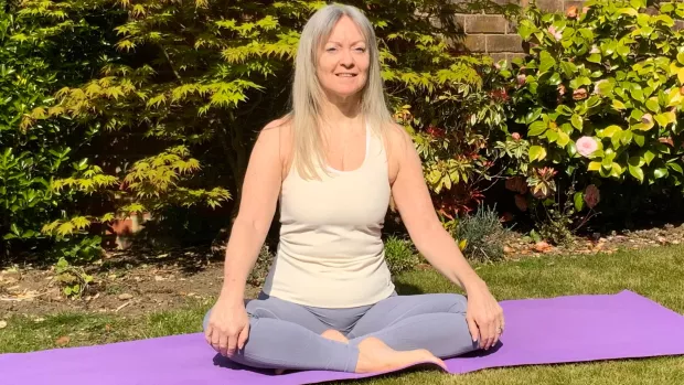 The photo shows Tracy sitting cross-legged on a purple yoga mat in her garden