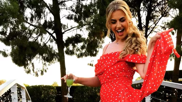 Yazzie stands smiling in a red polka dot dress with a cocktail on one hand.