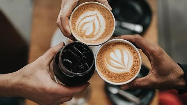 The photo shows three people holding their coffee cups together