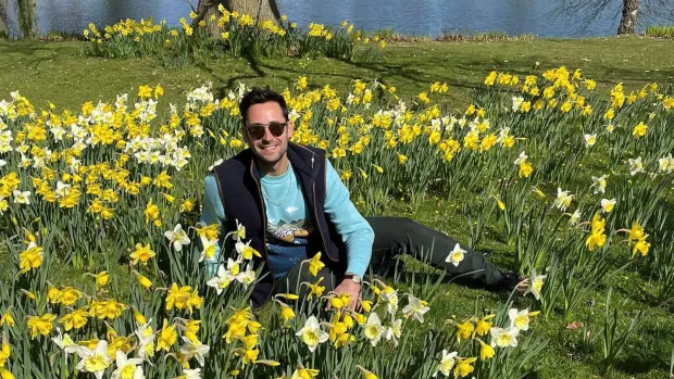 Tom sits in a grassy area surrounded by daffodils