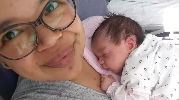 Sasha is lying in a hospital bed with her newborn baby daughter asleep on her chest.
