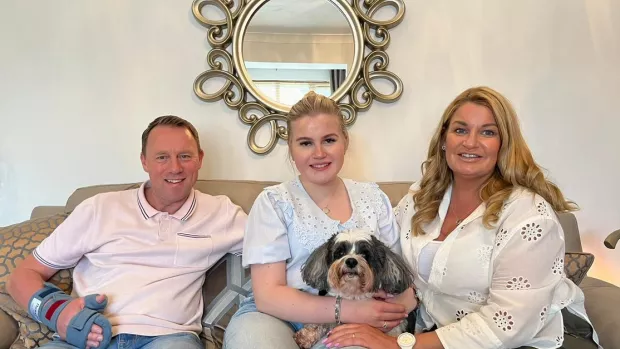 Stuart, Lucy and her mum sit on the sofa smiling with their dog