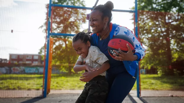 A smiling woman holds onto her child and holds a basketball