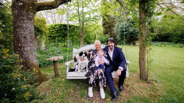 The photo shows Laurence and Jackie Llewelyn-Bowen and their baby granddaughter sitting together on a swing in their garden.