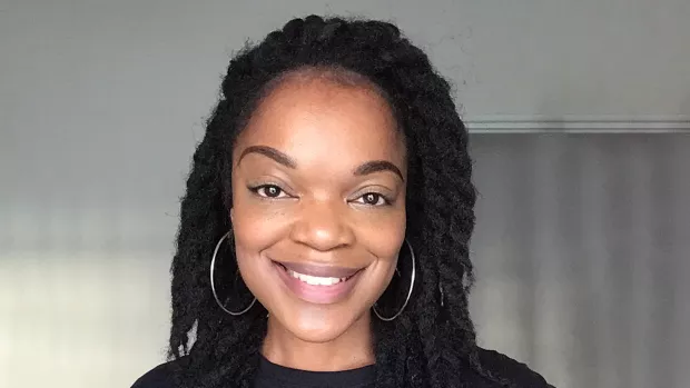 Natalie smiles to camera wearing hoop earings and braided hair