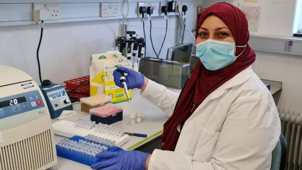 The photo shows Raghda sitting in the lab next to test tubes and other equipment