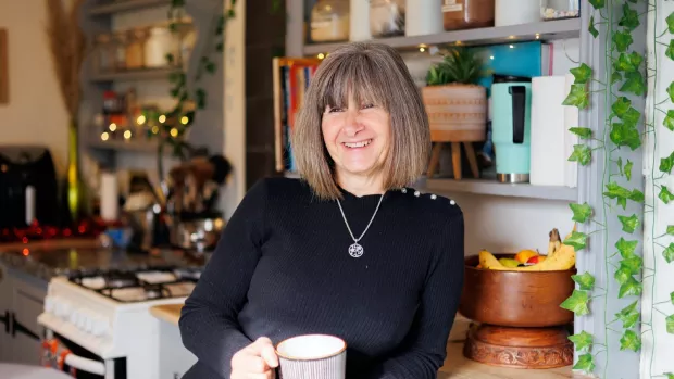 Linnetta is smiling and leaning against a kitchen worktop, holding a large mug.