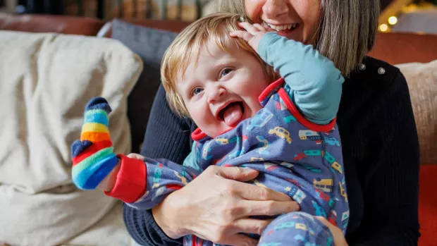 Linnetta is sitting on the sofa, playing with her grandson in her lap