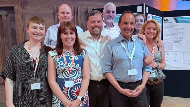 Emma is standing with the Register team at an MS conference 