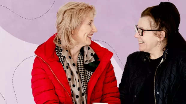 White woman wearing red jacket chats to a White woman with dark hair and glasses