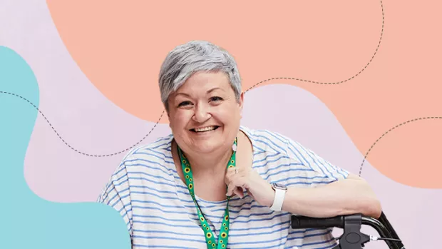 White lady with grey hair wearing a sunflower lanyard using a wheelchair