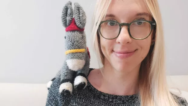 Heather smiles to camera. A small knitted donkey named Dizzy sits on her shoulder.