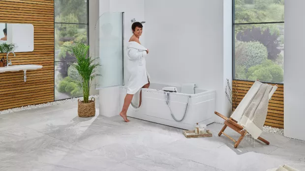 A woman is stepping into an accessible bath in her accessible bathroom.