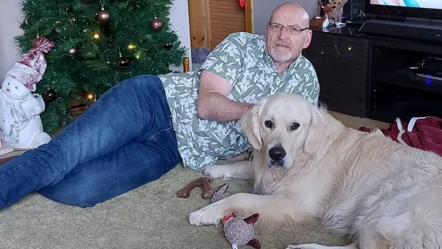 Iain Clark lies on the living room floor behind Golden Retriever Obi