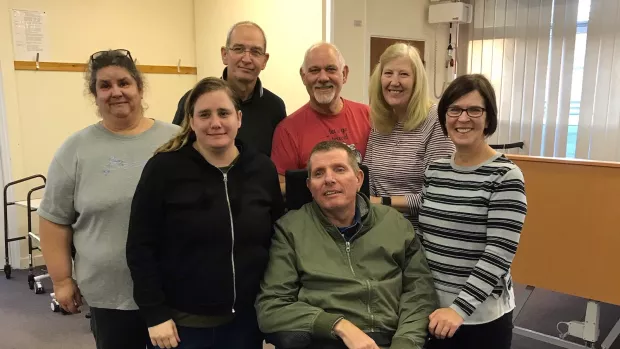 Six people are grouped around a man in a wheelchair