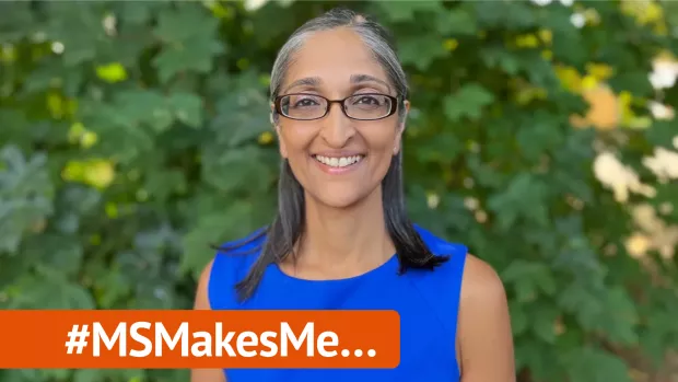 Trishna is wearing a blue dress and glasses. She is outside with green foliage behind her. A banner overlaid on the photo reads #MSMakesMe