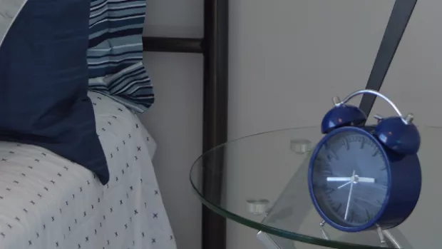 A blue alarm clock next to a bed