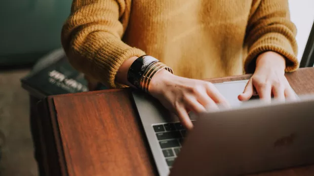 A woman is sitting at a desk, typing on a laptop